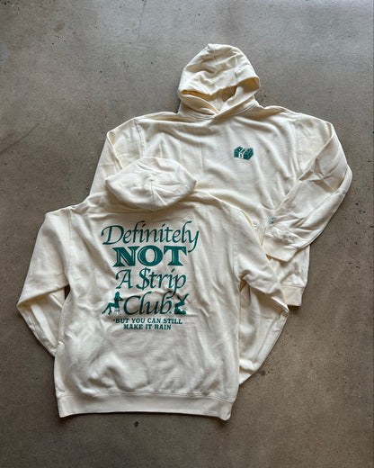 An off-white hooded sweatshirt laid flat on a concrete floor, showing a large teal graphic on the back that reads 'Definitely NOT A Strip Club' with smaller text below, and a small teal chest logo on the front.