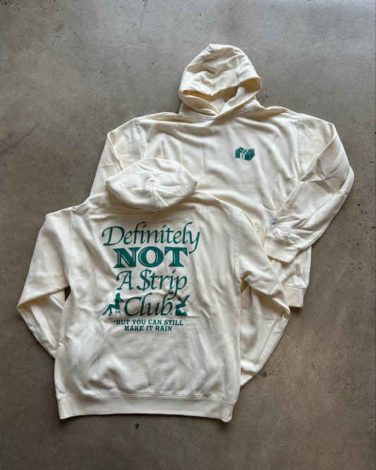An off-white hooded sweatshirt laid flat on a concrete floor, showing a large teal graphic on the back that reads 'Definitely NOT A Strip Club' with smaller text below, and a small teal chest logo on the front.