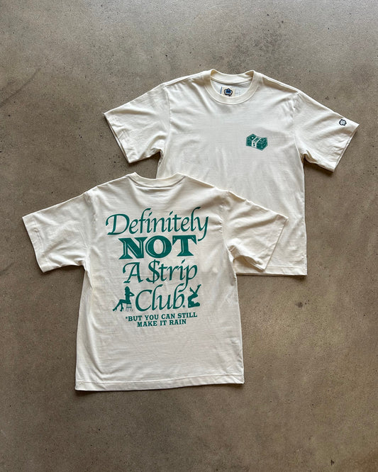 Two off-white t-shirts laid flat on a concrete floor. The front shirt shows a large green graphic text reading 'Definitely NOT A Strip Club' with smaller text below, and the back shirt has a small green chest graphic.