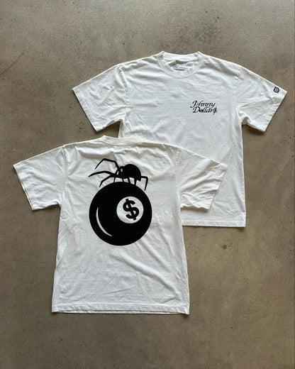 Two white short-sleeve T-shirts laid flat on a concrete floor. The front shirt shows a large black graphic of a spider on a billiard ball with a dollar sign, and the back shirt has small black script text on the chest reading 'Johnny Decker'.