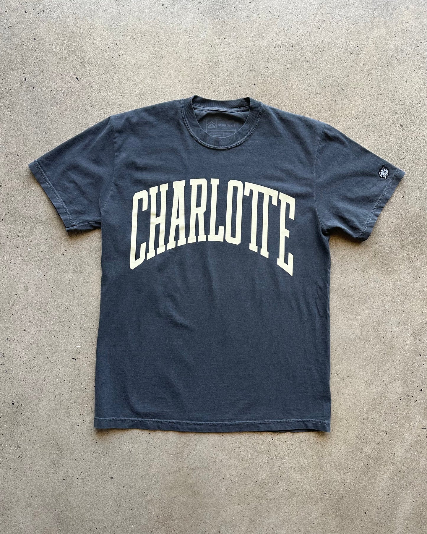 Navy blue t-shirt with 'Charlotte' printed in white on a concrete floor.