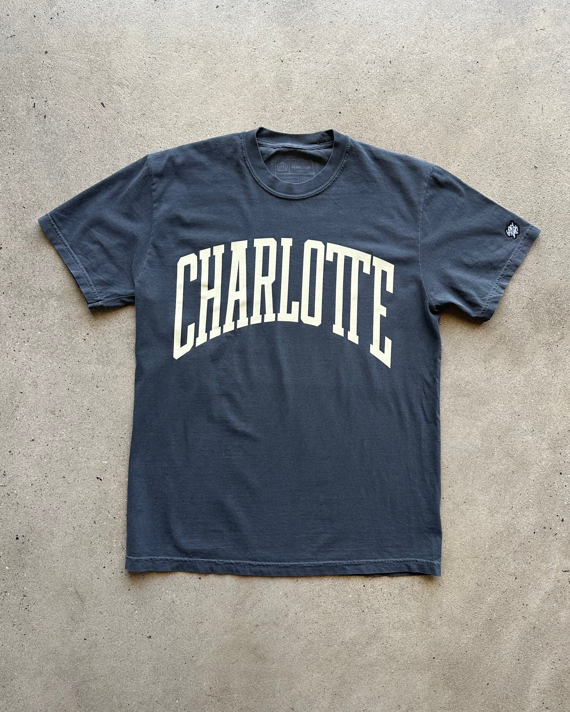 Navy blue t-shirt with 'Charlotte' printed in white on a concrete floor.