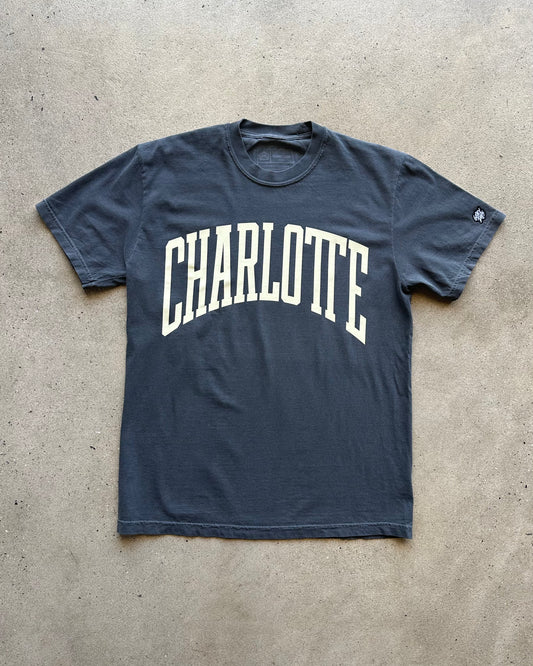 Navy blue t-shirt with 'Charlotte' printed in white on a concrete floor.