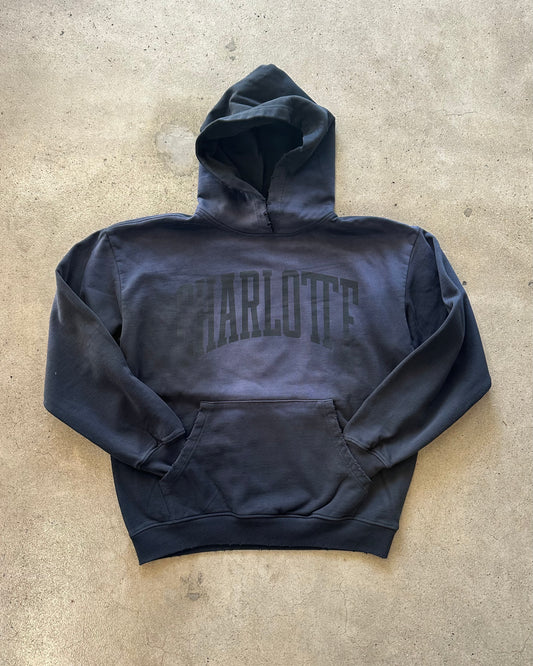 Black hoodie with 'Harlute' text on a beige surface