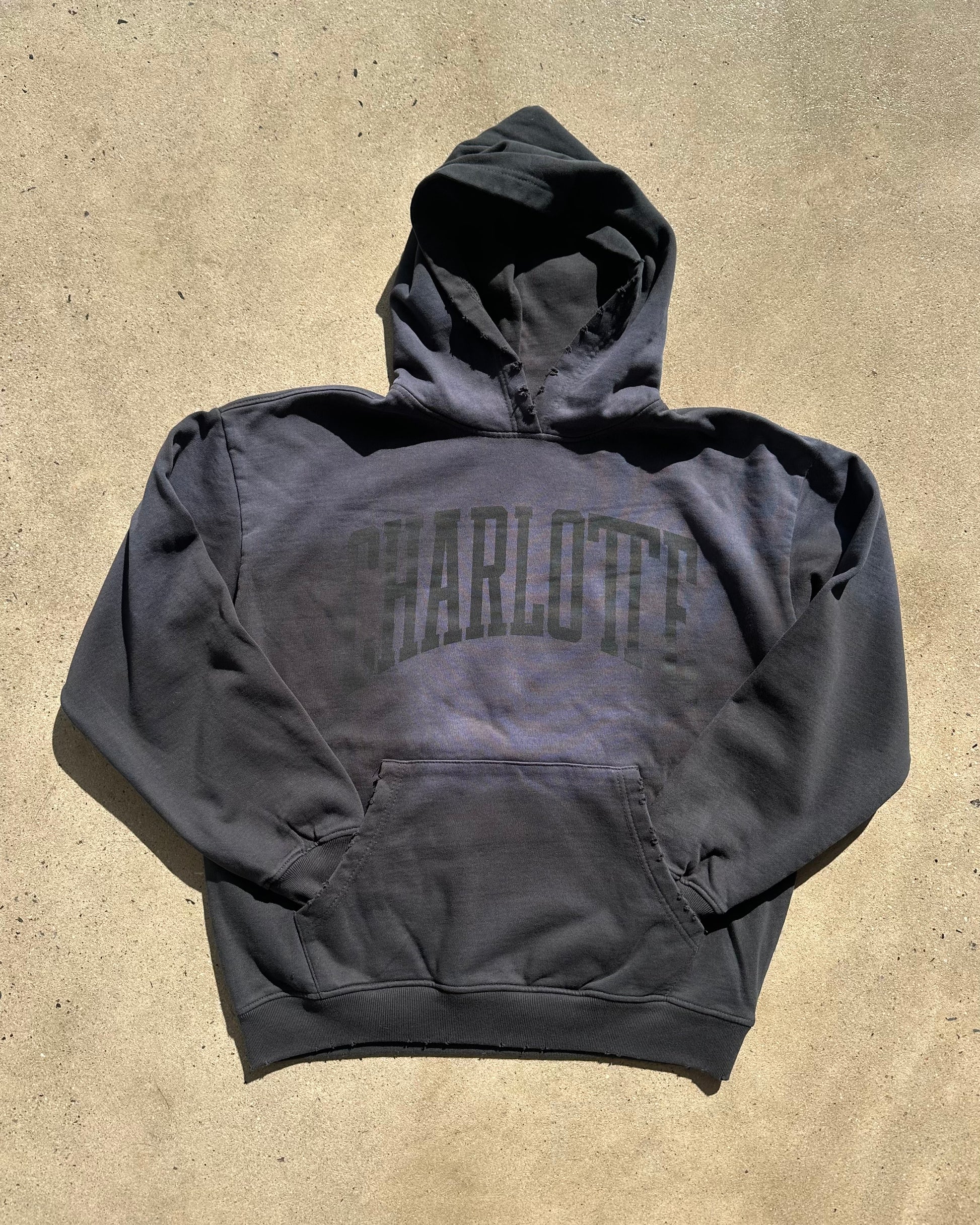 Black hoodie with 'Charlotte' text on a beige surface
