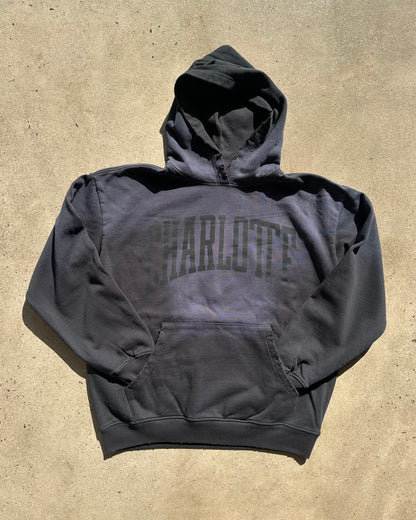 Black hoodie with 'Charlotte' text on a beige surface