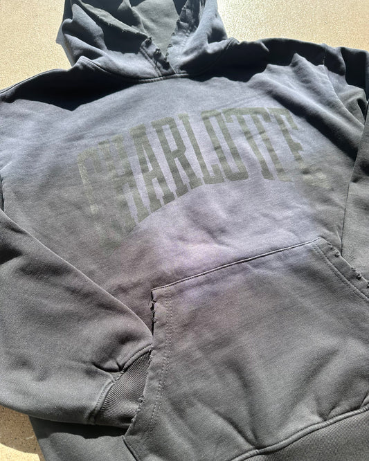 Gray hoodie with 'Charlotte' text on a beige surface